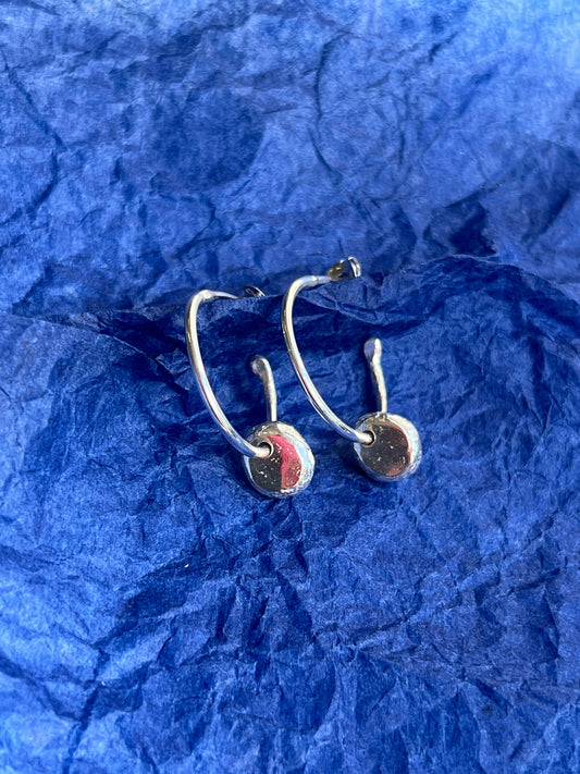 Silver earrings with hammered dangle drops on a blue textured paper background