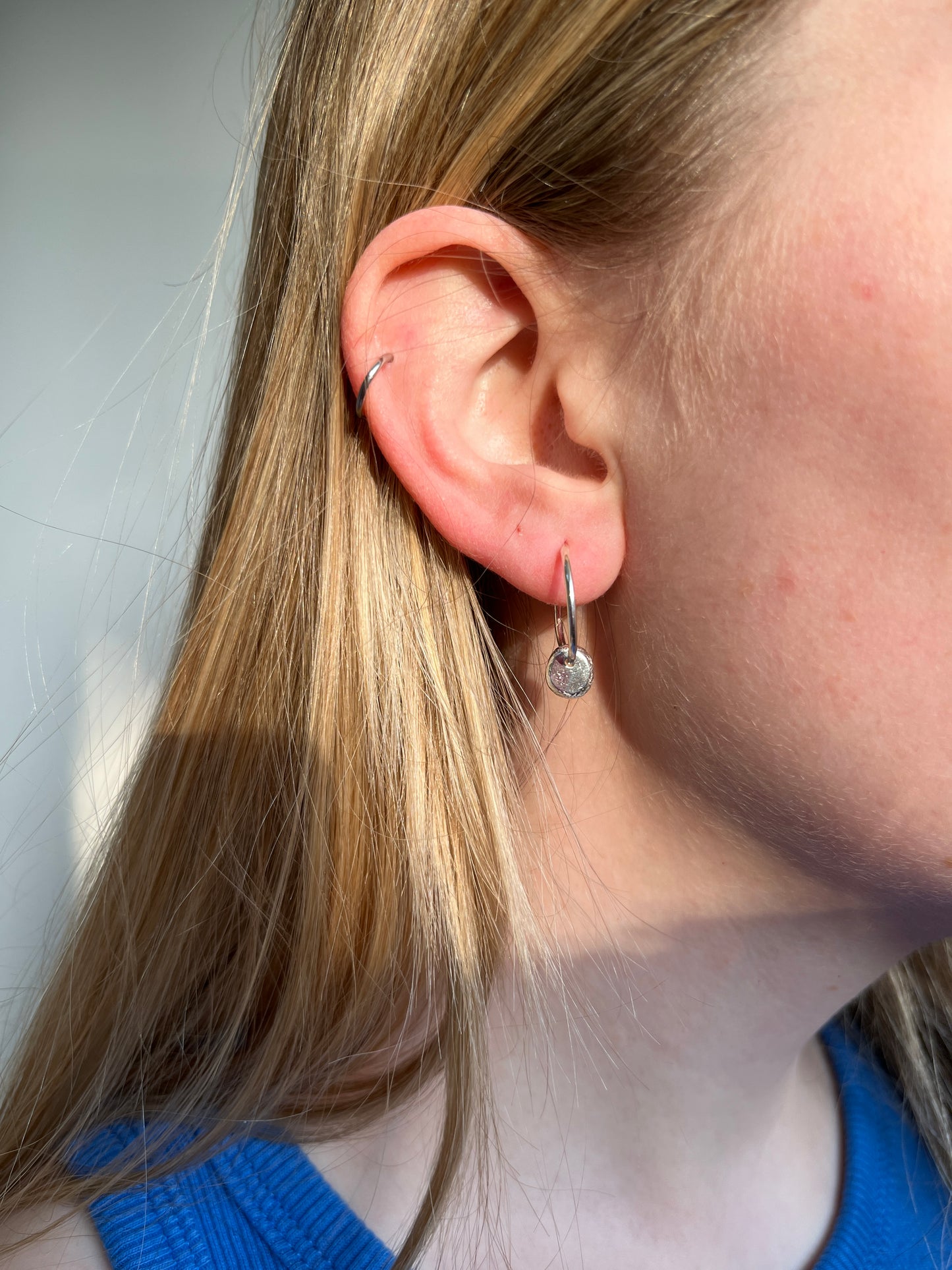 A close-up image of a woman's ear wearing a silver hoop earring with a dangly silver pebble design.