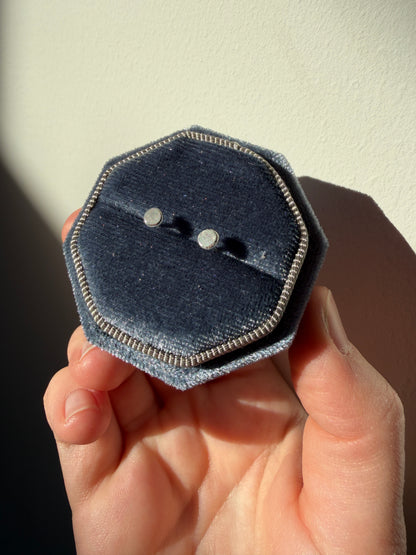recycled silver studs in a blue velvet box held infront of a white wall at an angle