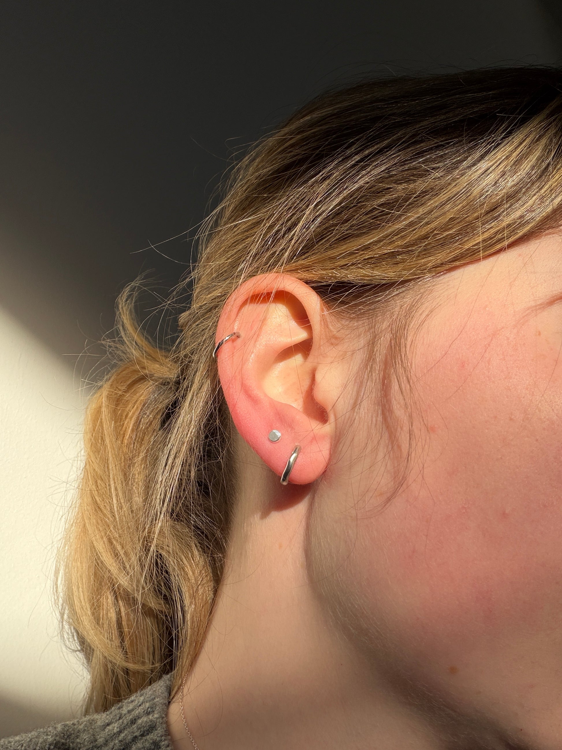 recycled silver studs pictured in a stack of piercings in a girl's ear in front of a white wall