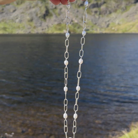 Handmade silver chain necklace with white, freshwater pearls and a t-bar clasp, pictured against a lake