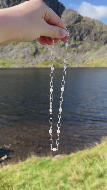Handmade silver chain necklace with white, freshwater pearls and a t-bar clasp, pictured against a lake