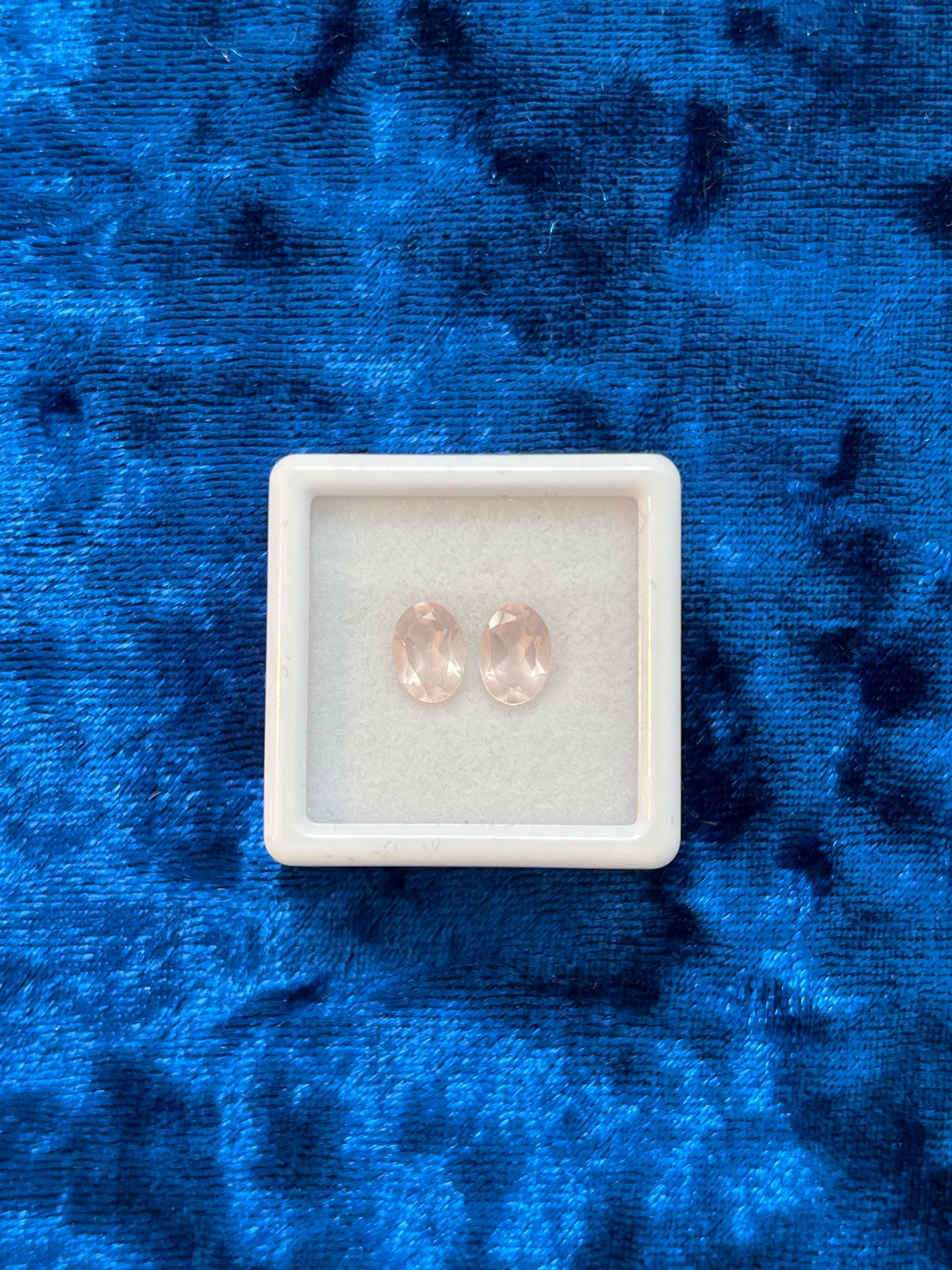 Pair of rose quartz gemstones in a white box on a blue textured background