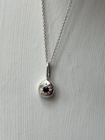 a sterling silver pendant with a star set sapphire gemstone on a silver trace chain, pictured against a white background.