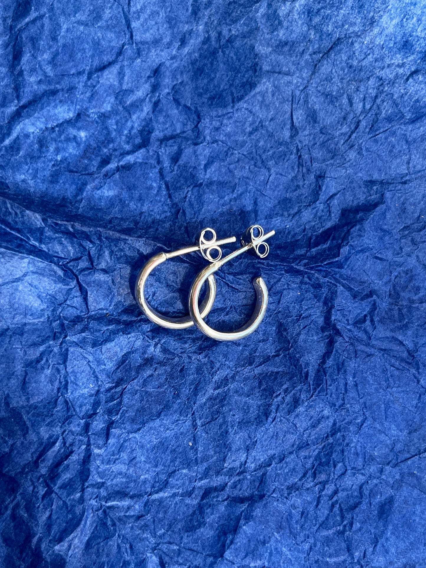 Silver hoop earrings on a blue crumpled paper background