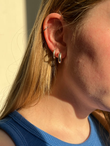 Close-up of an ear with the simple hoop earrings styled in a stack, on a girl wearing a blue top.