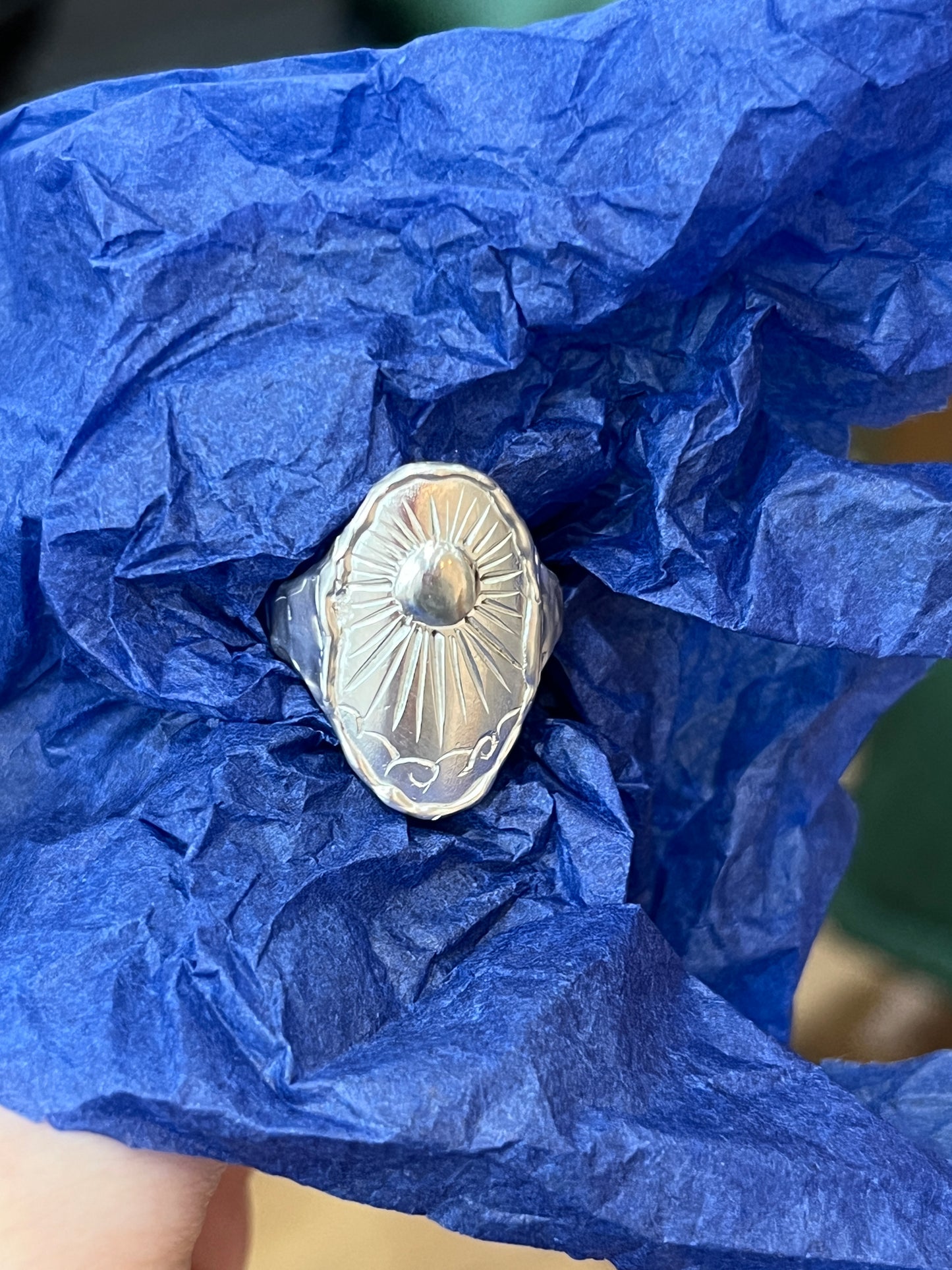 A sterling silver ring with an intricate beaming sun engraving and molten band design, displayed with a blue background.