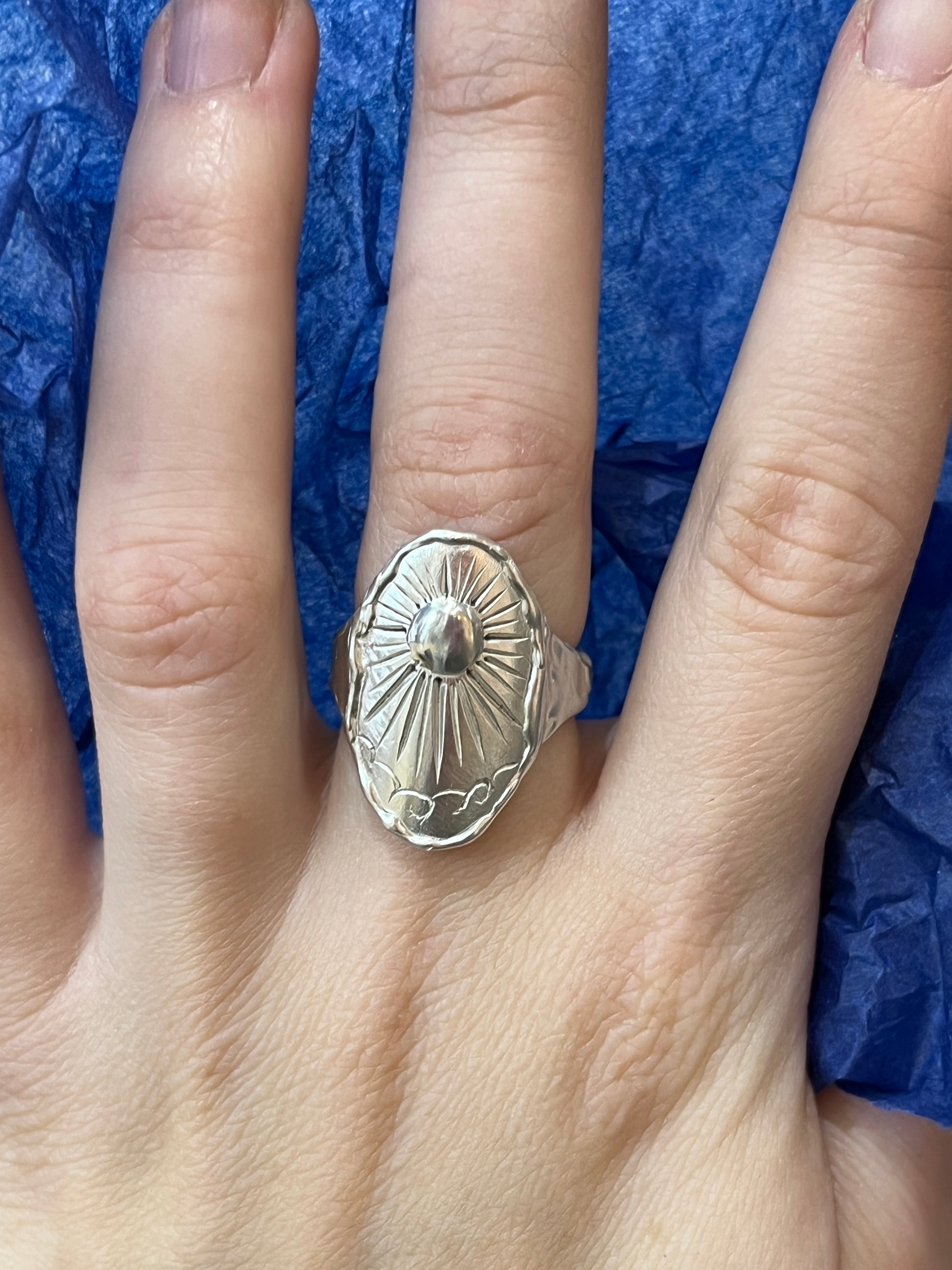 A sterling silver ring with an intricate beaming sun engraving and molten band design, displayed on a hand showing the fit.