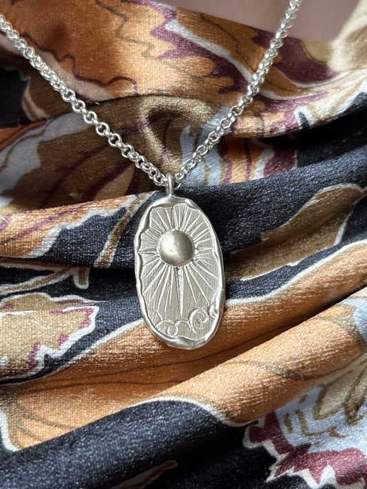 sterling silver pendant with solstice design pictured against golden velvet fabric.