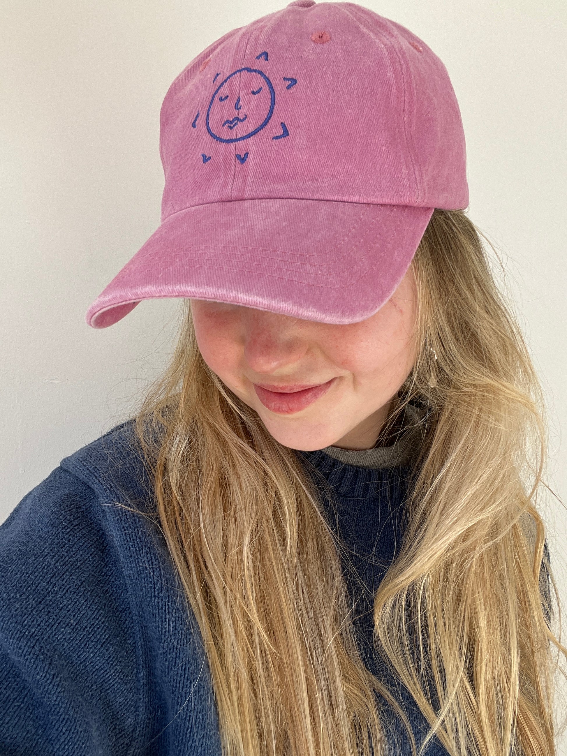 A person wearing a pink baseball cap with the sun.slices logo on the front.