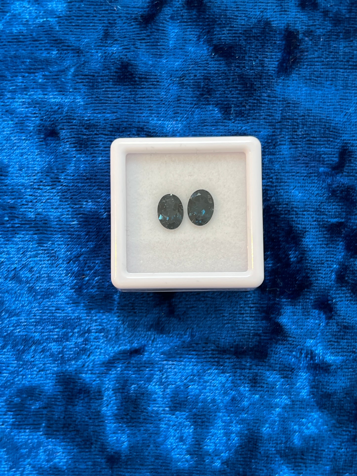 Two dark teal stones in a white square container on a blue textured background