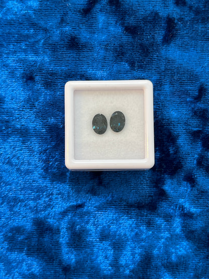 Two dark teal stones in a white square container on a blue textured background