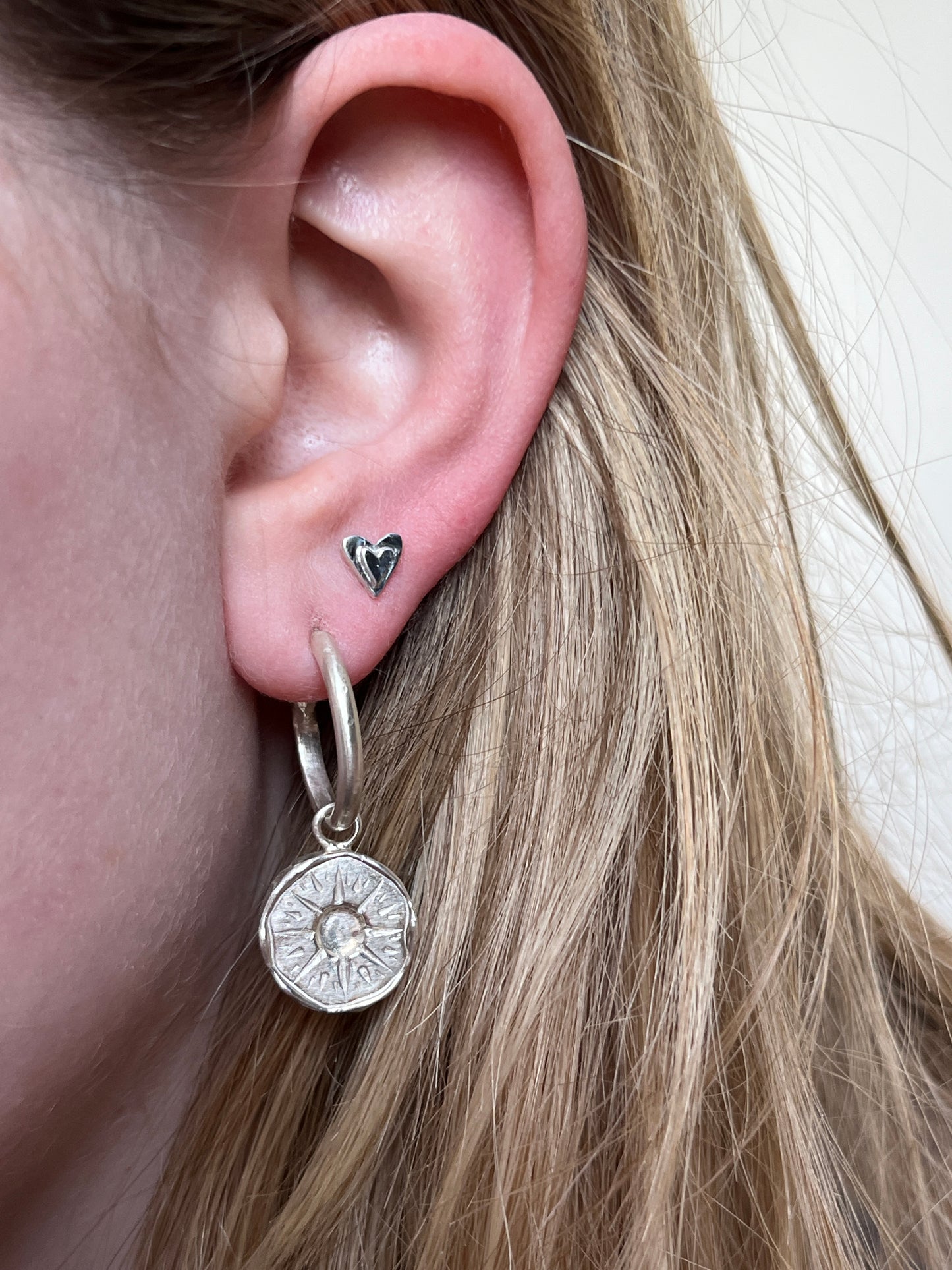 A close-up image of a person's ear wearing a silver heart stud earring in the second piercing